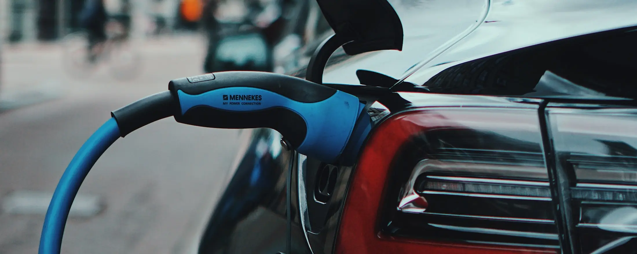 A blue Type 2 connector plugged into a car's charging port on a city street.